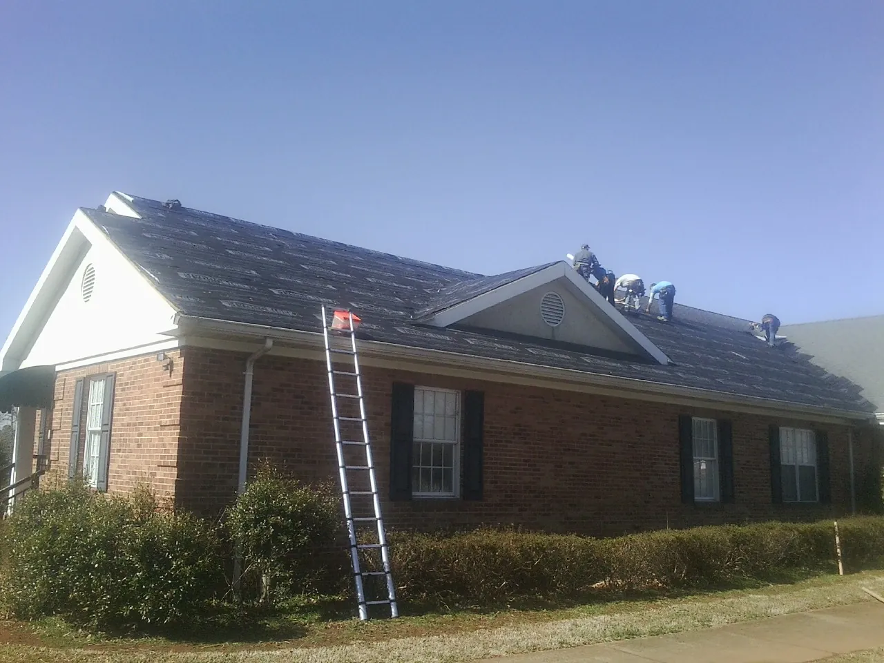 Crew tearing shingles off a brick ranch roof with a ladder set — Metal Roof Repair work by our crew in Suches