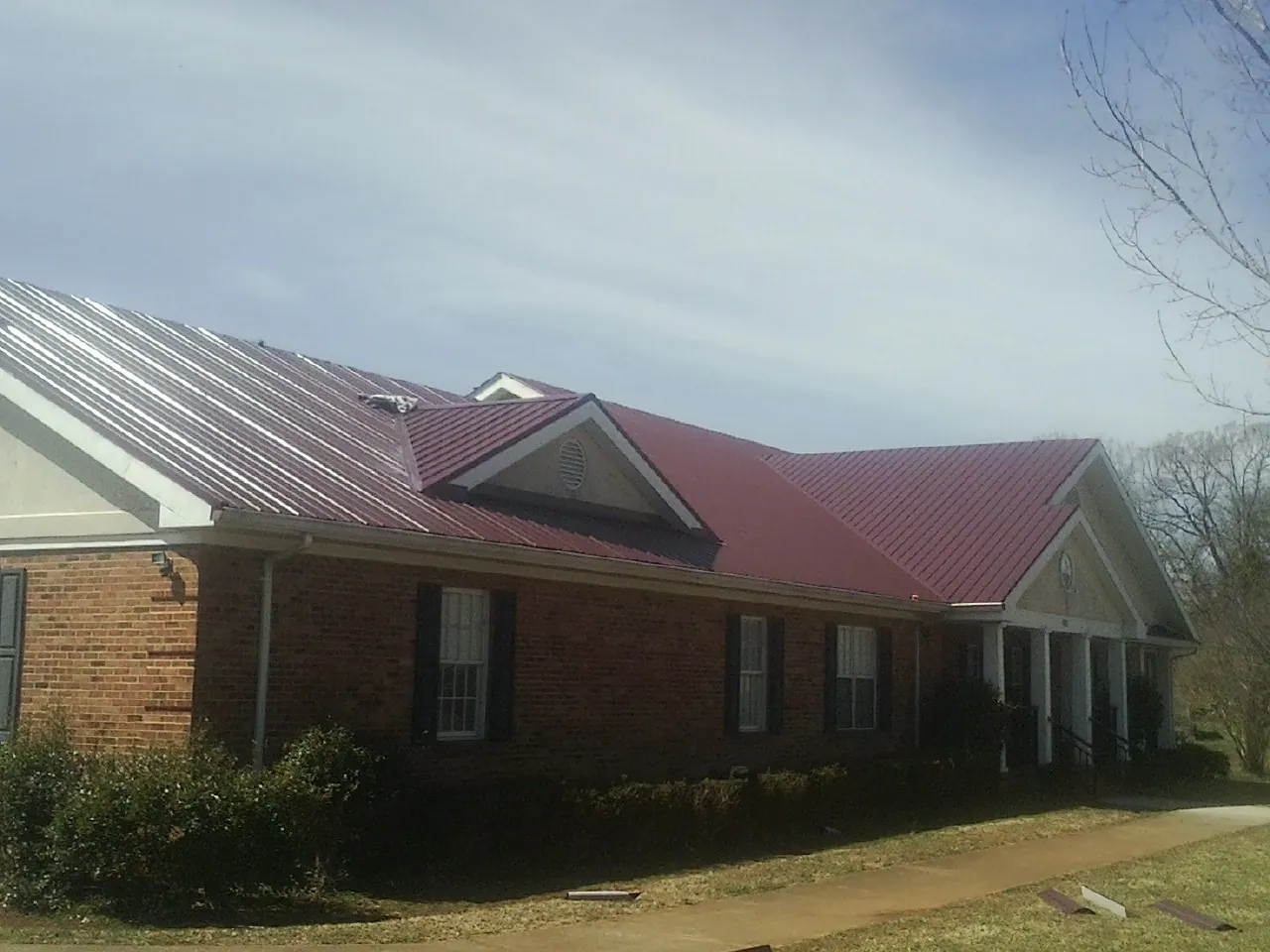 Red metal roof with gabled entries on a long brick building, from a Hail Damage Roof Repair job in Suches