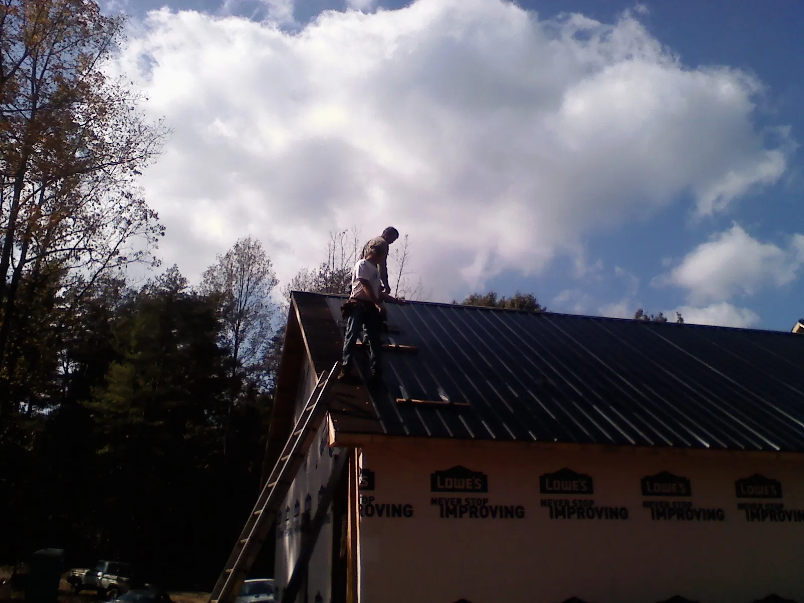 Roofer fastening dark metal panels high against a cloudy sky, from a Roof Inspection job in Suches