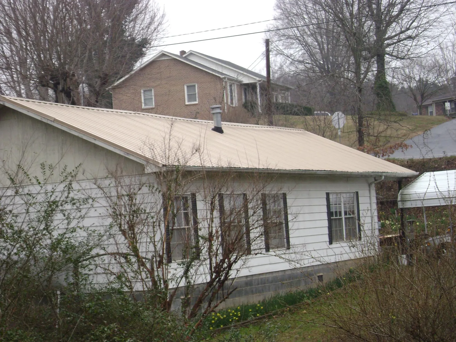 Tan metal roof on a white sided house set into a hillside — Commercial Roofing by Roofing Brothers in Suches